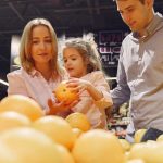 Parents and child selecting fresh oranges together at the supermarket. Captures family bonding and healthy shopping.